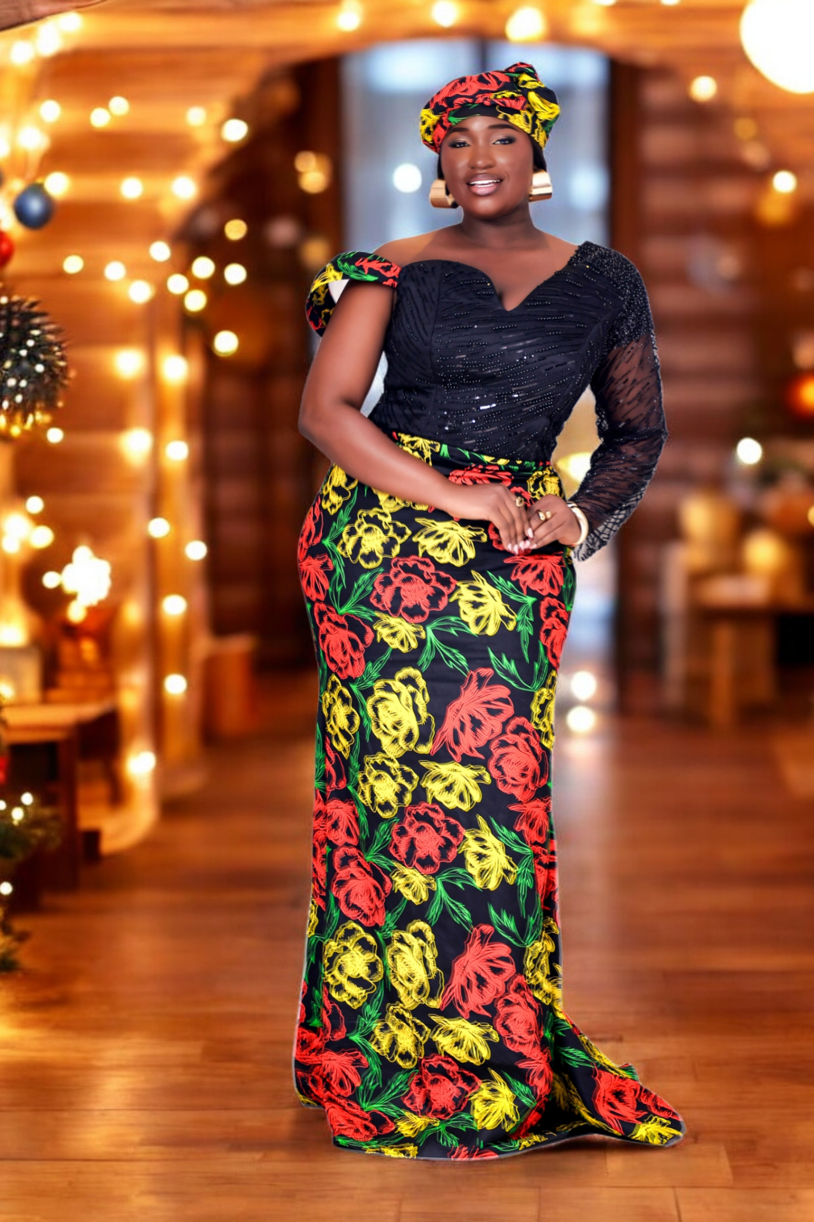 Women in a colorful floral African Print dress with embellished hand beaded upper bodice in black with headwraps standing in front of a decorated Christmas tree and fireplace.