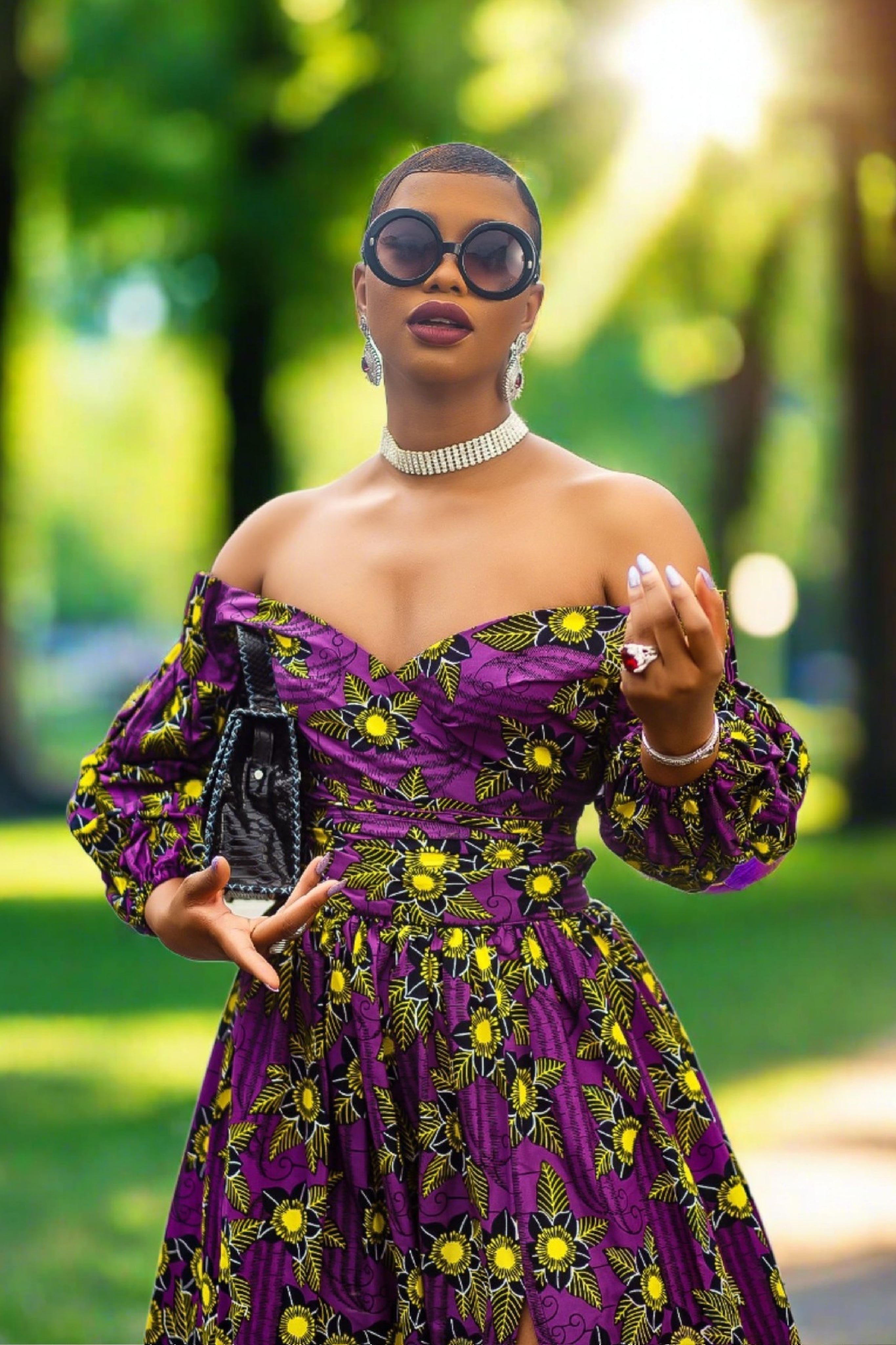 A woman wearing a bold African print Ankara purple and yellow African print wrap top with bubble sleeves and a off-the-shoulder neckline.