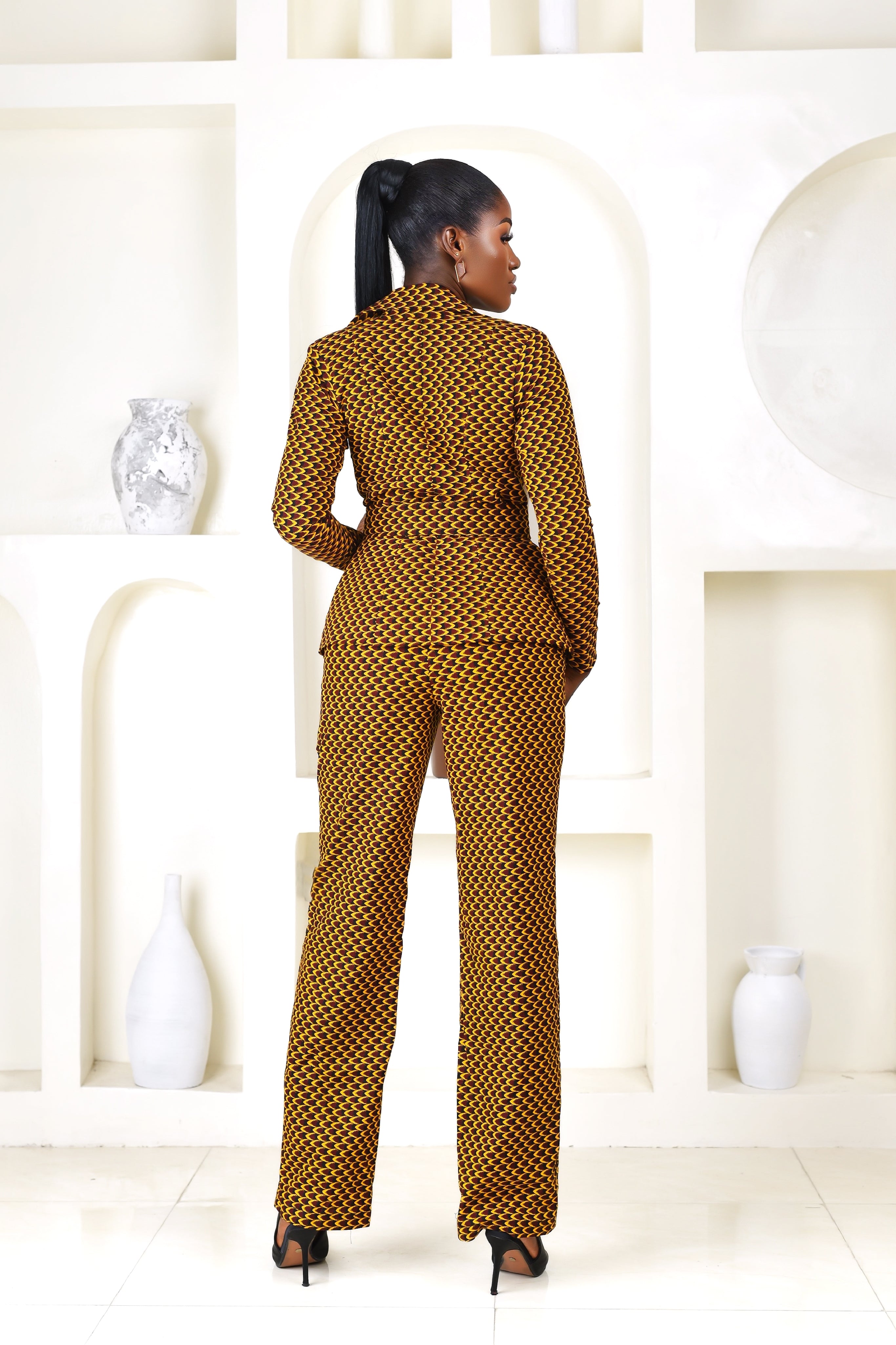 Woman in a patterned African Print Blazer and double breasted pantsuit set standing in a modern indoor setting with plants.