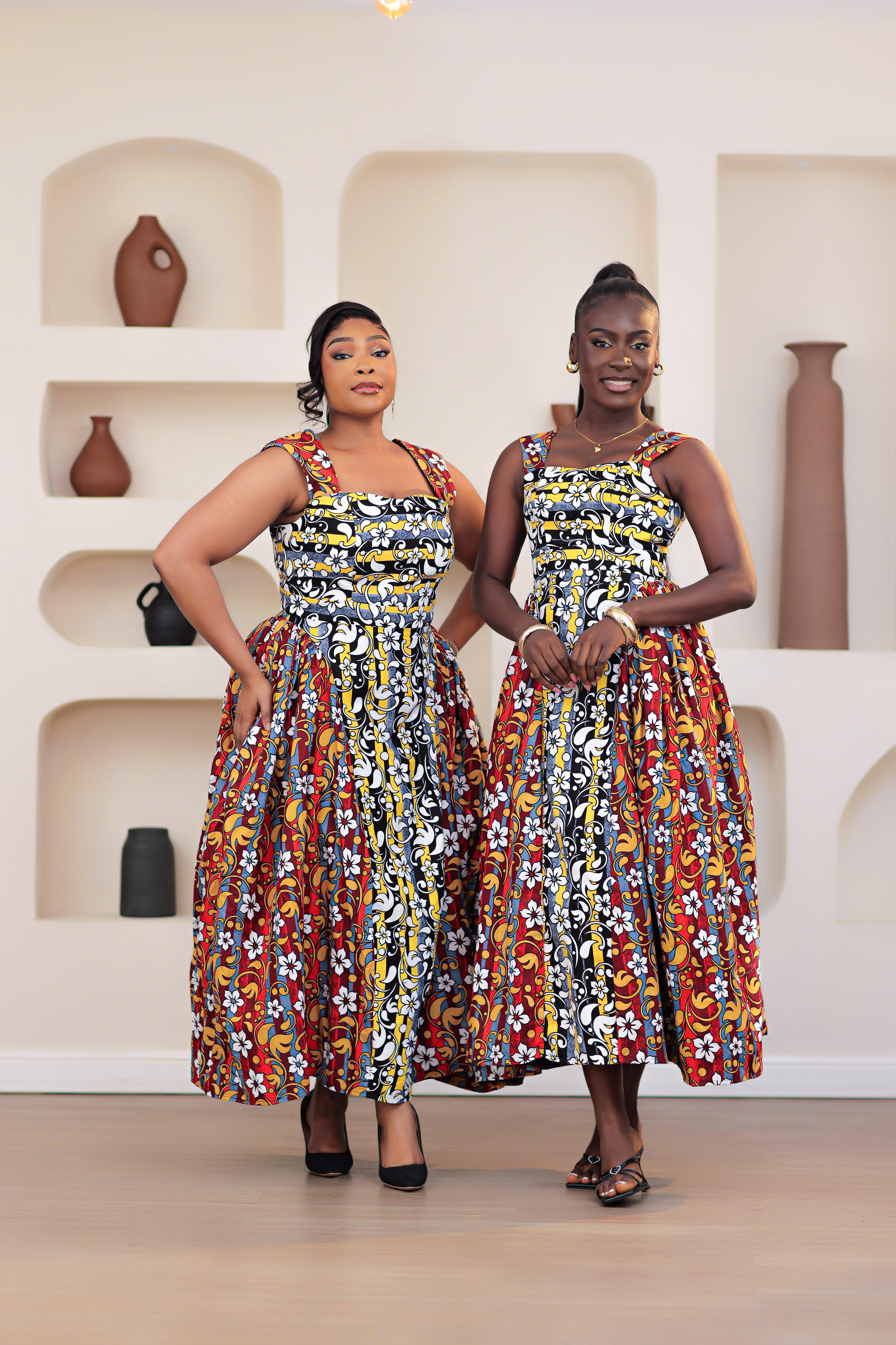 two women in a colorful patterned mixed prints african print ankara sleeveless dress standing in front of a decorative wall with shelves.