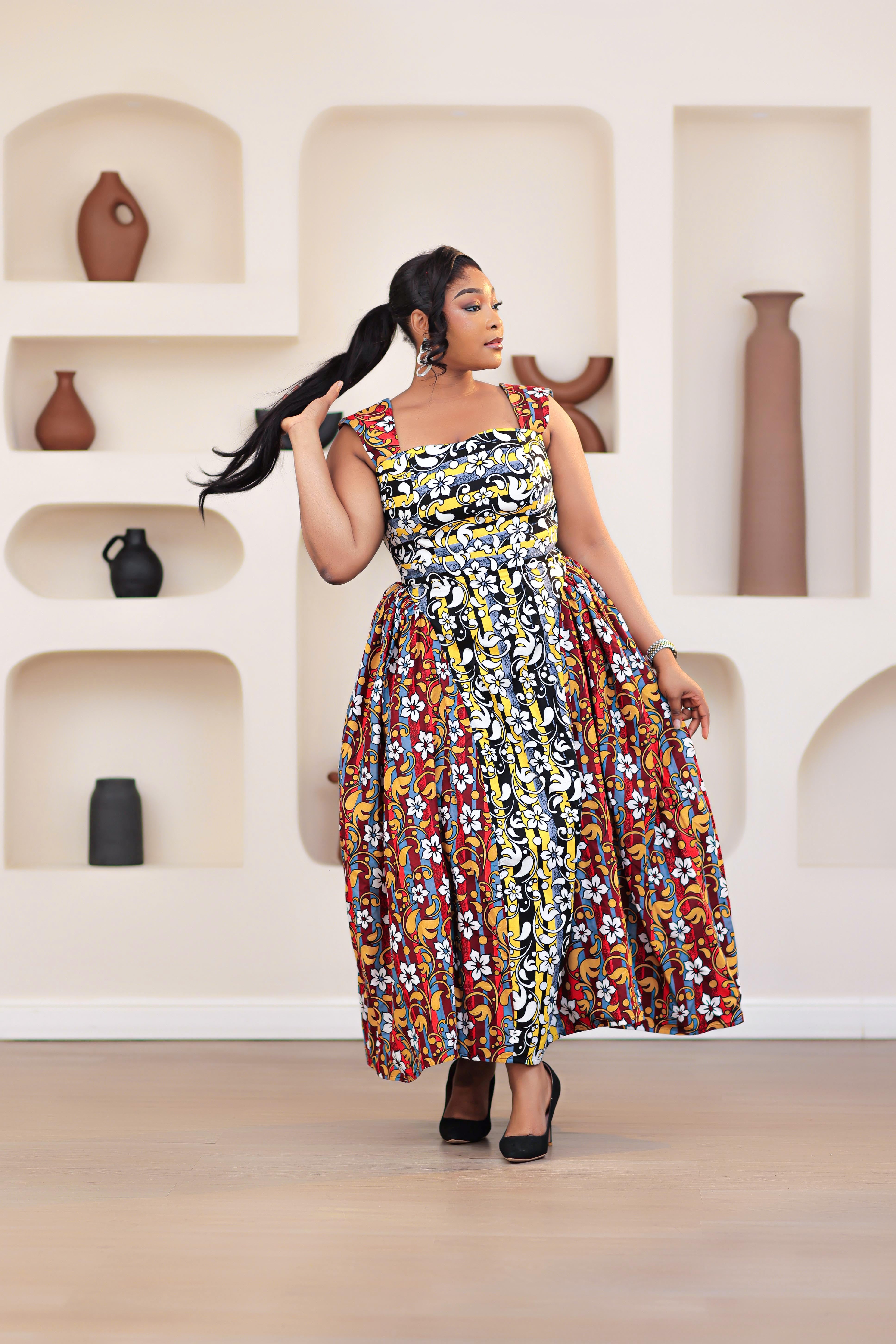 Woman in a colorful patterned mixed prints african print ankara sleeveless dress standing in front of a decorative wall with shelves.