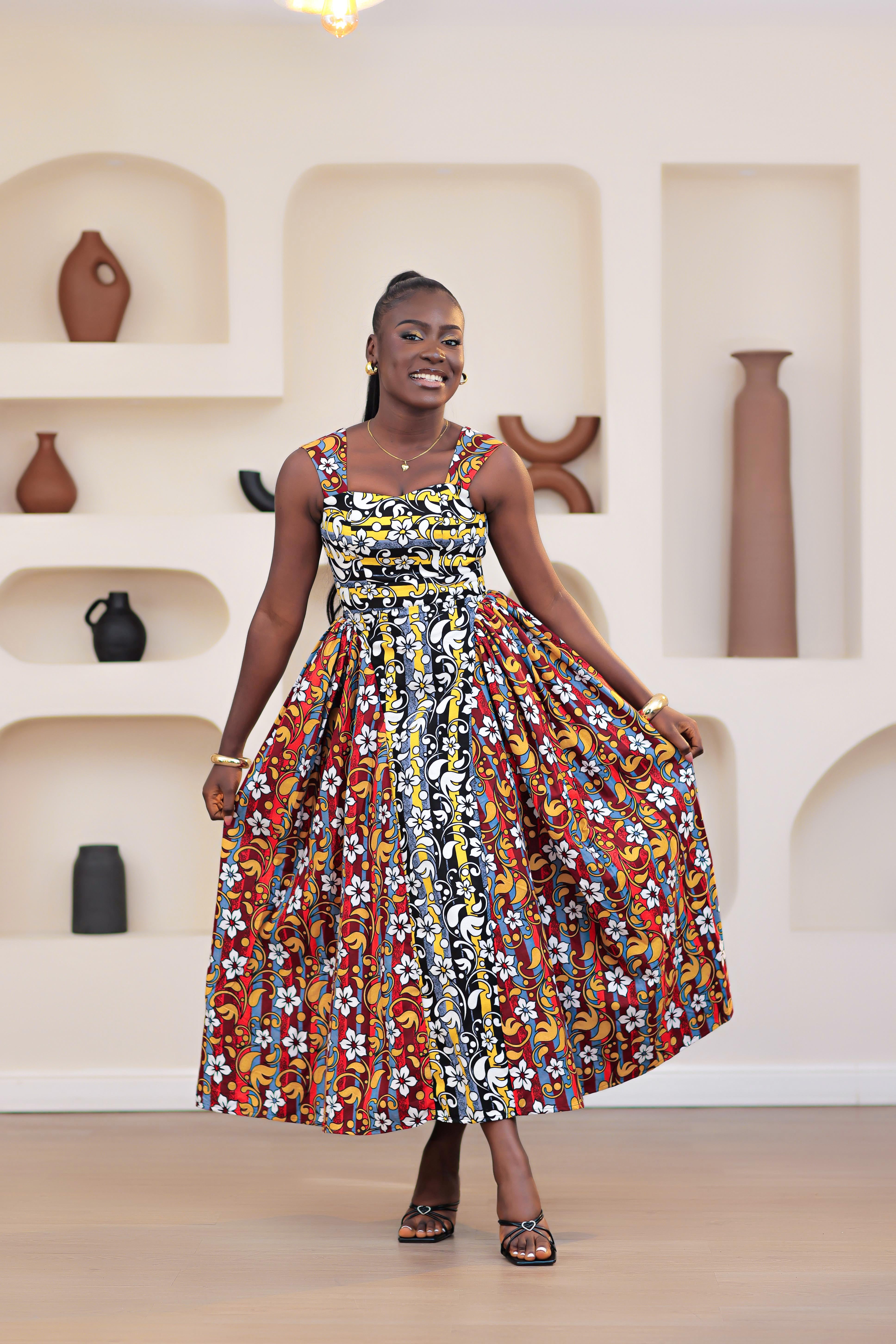 Woman in a colorful patterned mixed prints african print ankara sleeveless dress standing in front of a decorative wall with shelves.