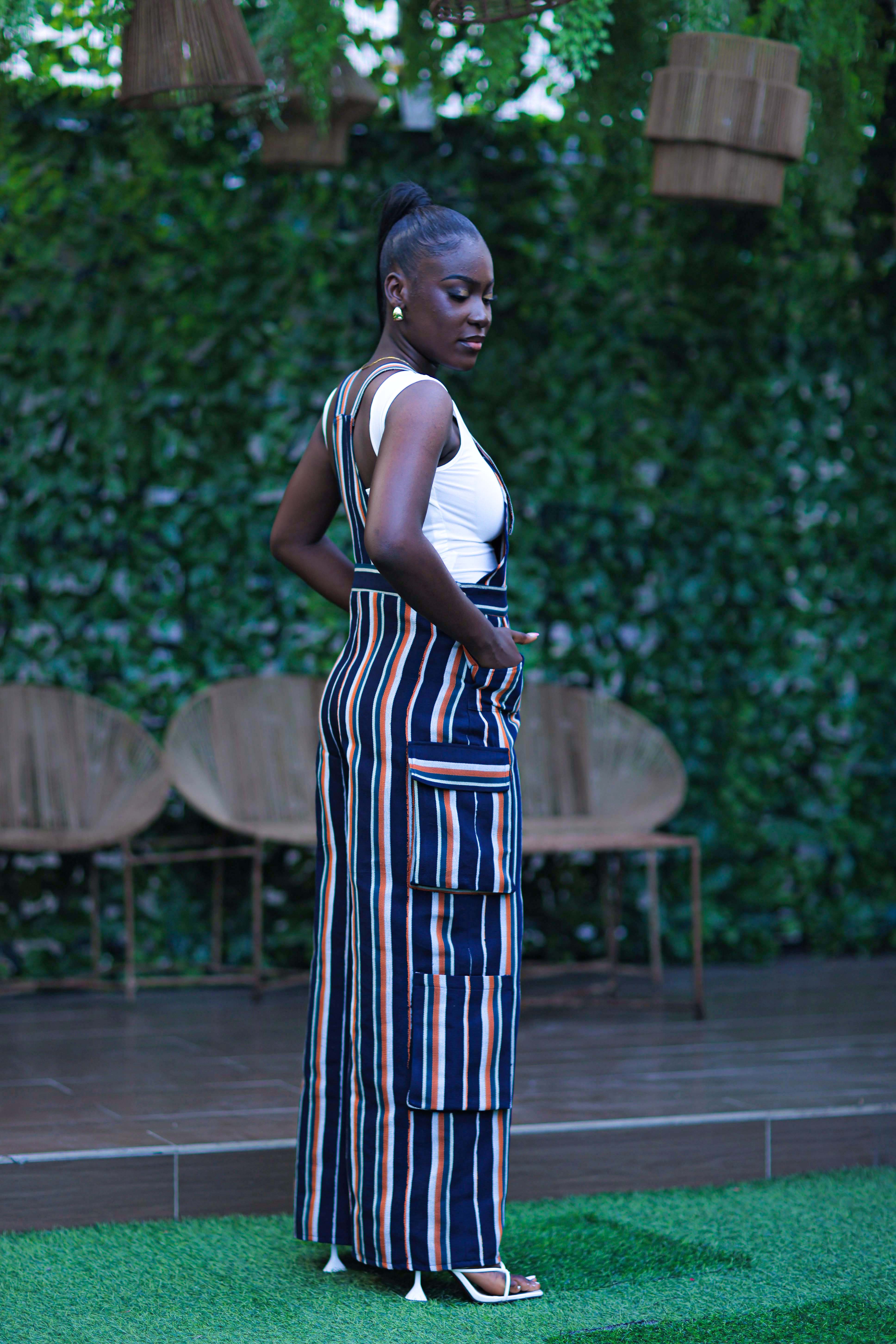 Woman in a striped jumpsuit standing outdoors with greenery in the background