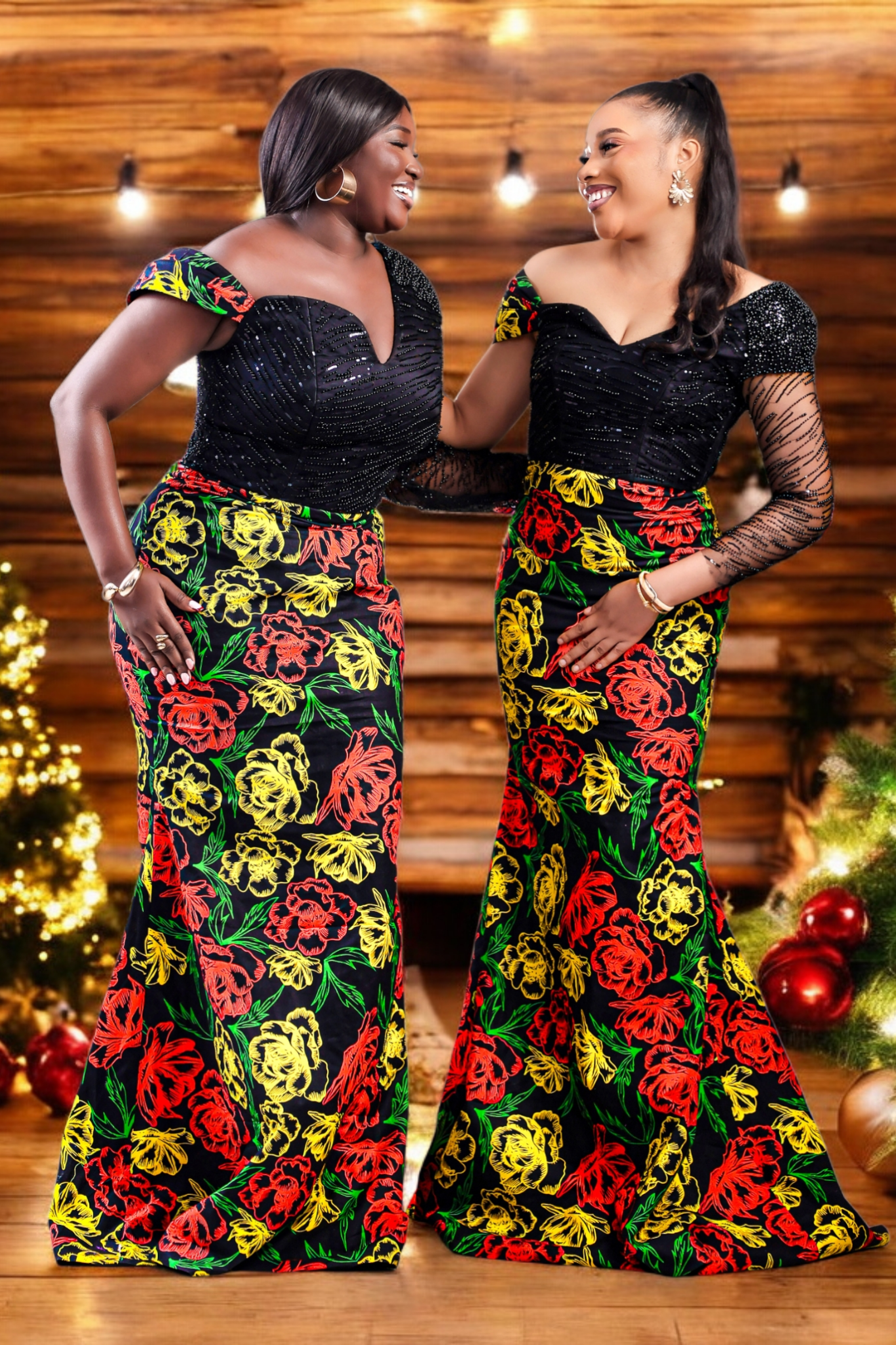 Women in a colorful floral African Print dress with embellished hand beaded upper bodice in black standing in front of a decorated Christmas tree and fireplace.