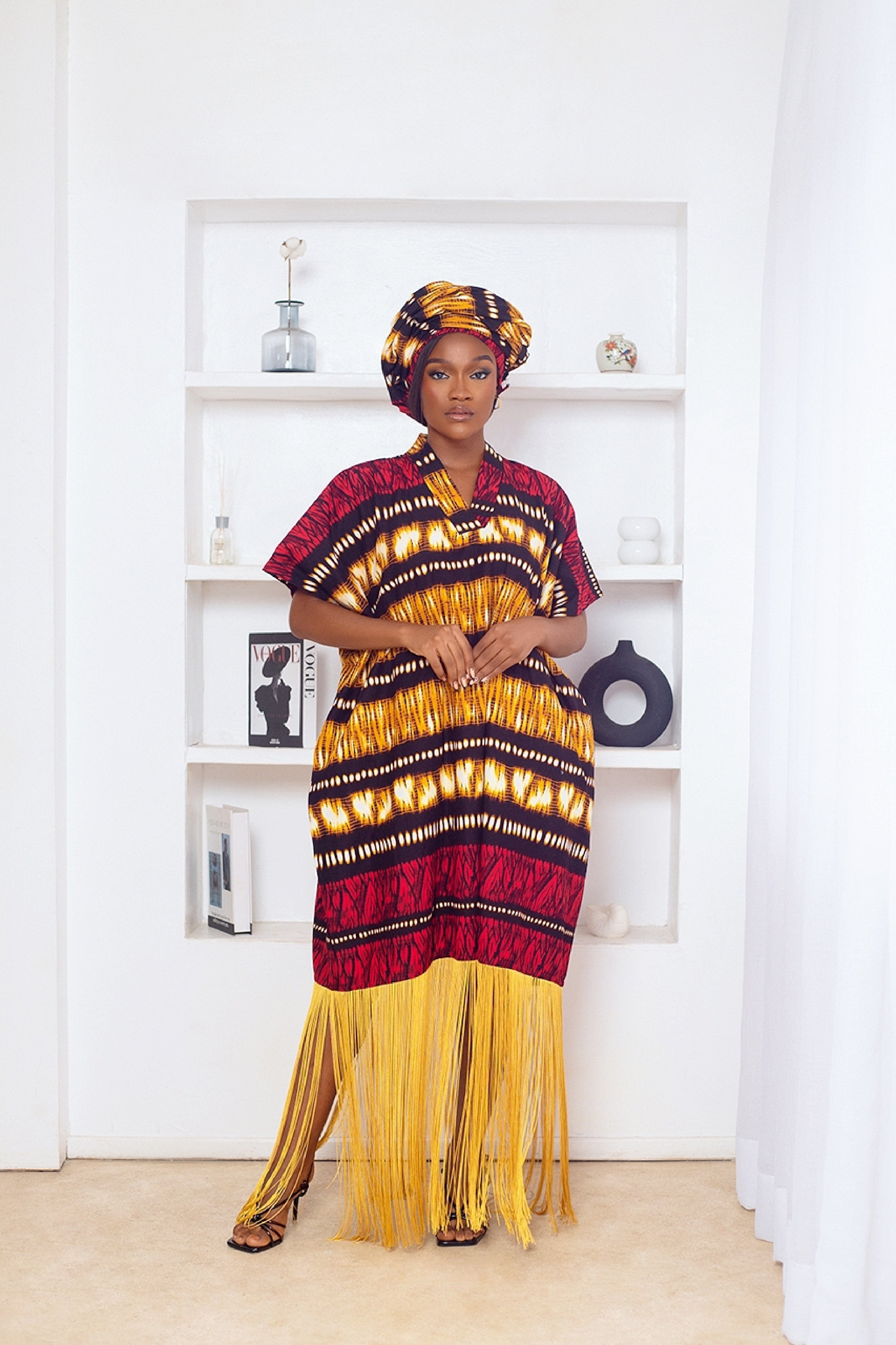 Woman in African Print Ankara Boubou dress outfit with headwrap, fringe and tassle details in red gold brown multicolor