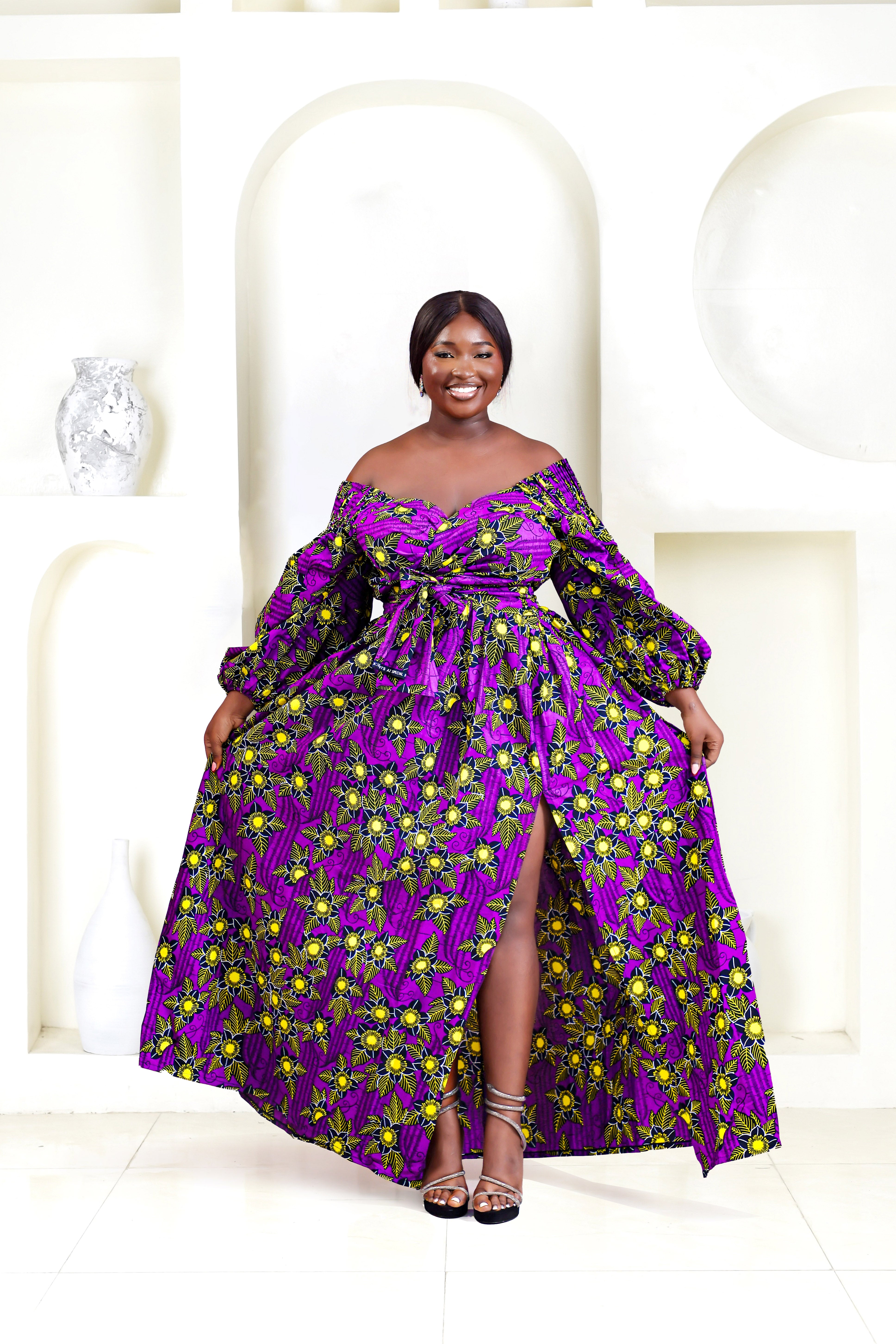 A woman wearing a purple and yellow African print wrap top with bubble sleeves and a thigh high slit skirt.