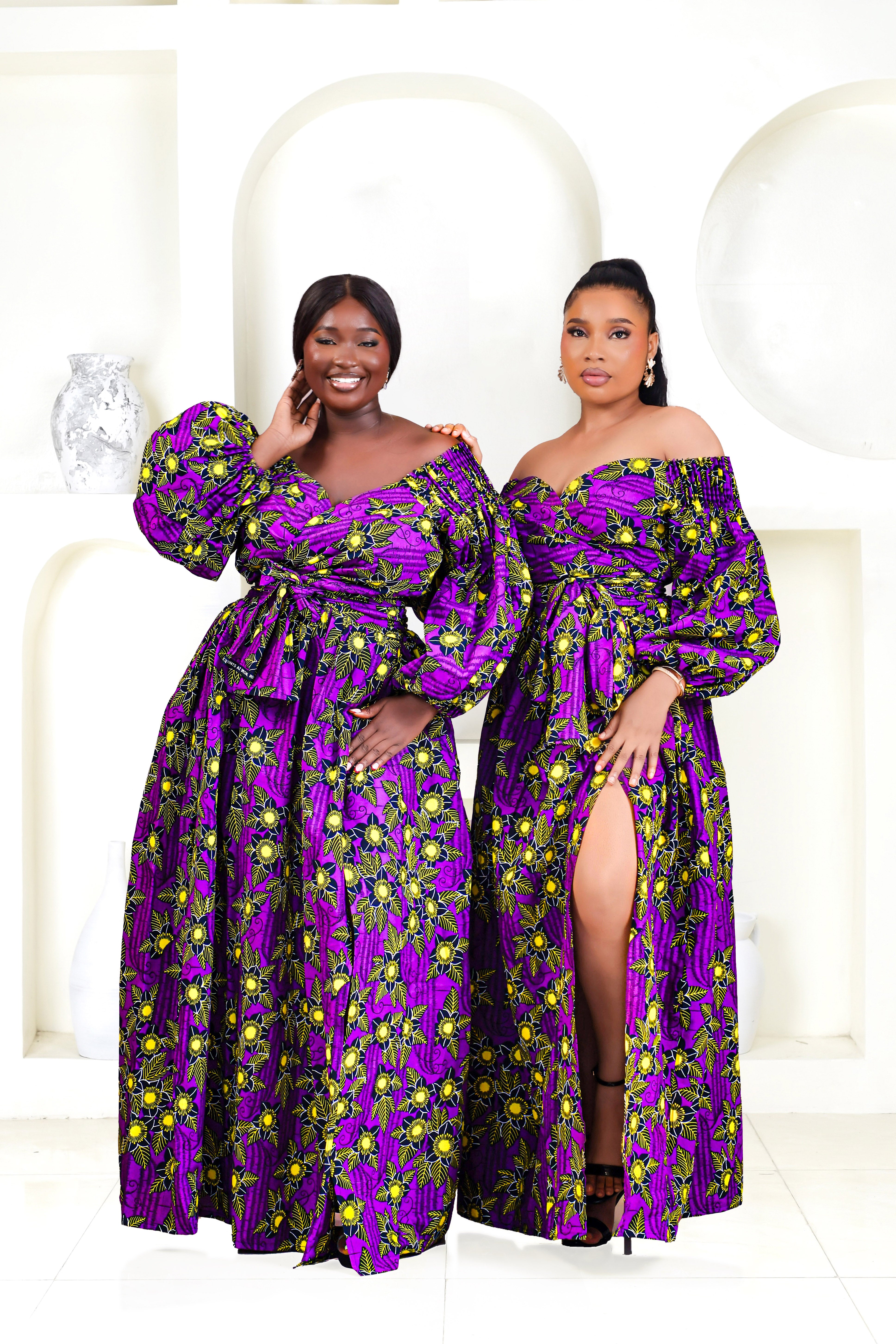 A woman wearing a bold African print Ankara purple and yellow African print wrap top with bubble sleeves and a off-the-shoulder neckline.