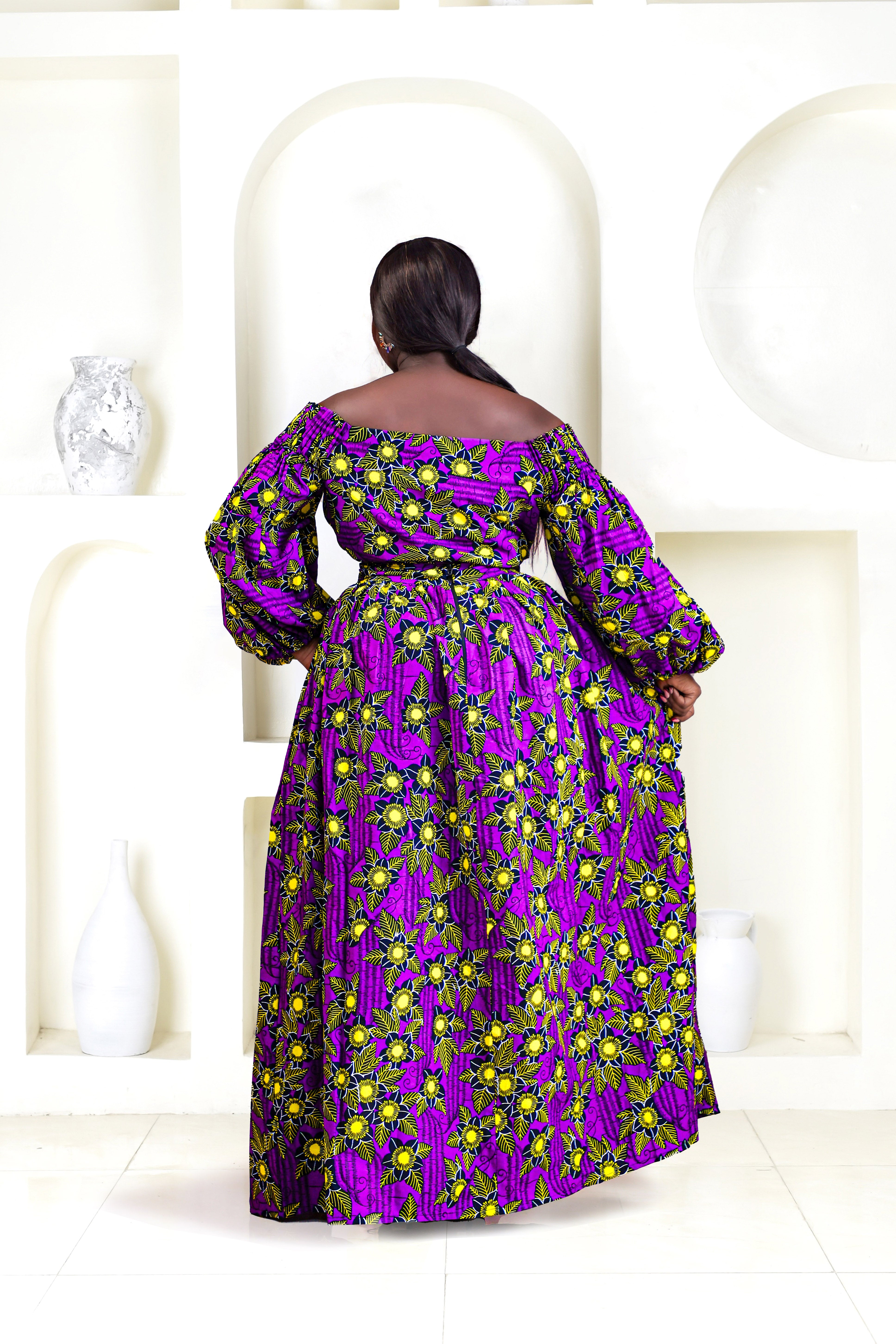 A woman wearing a bold African print Ankara purple and yellow African print wrap top with bubble sleeves and a off-the-shoulder neckline.