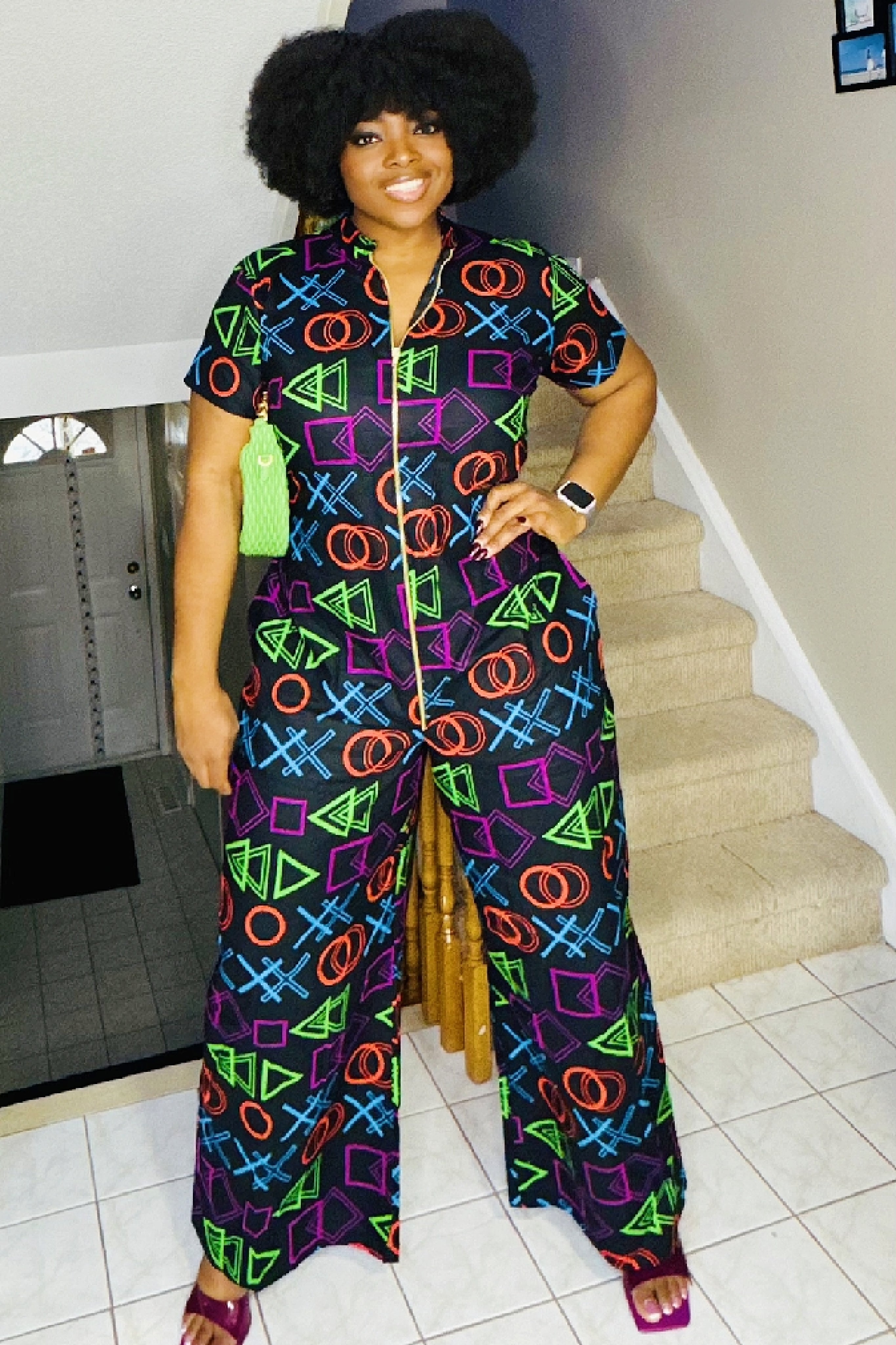A woman standing on a staircase wearing a colorful African print jumpsuit with a video game-inspired pattern, consisting of various geometric shapes in vibrant colors.