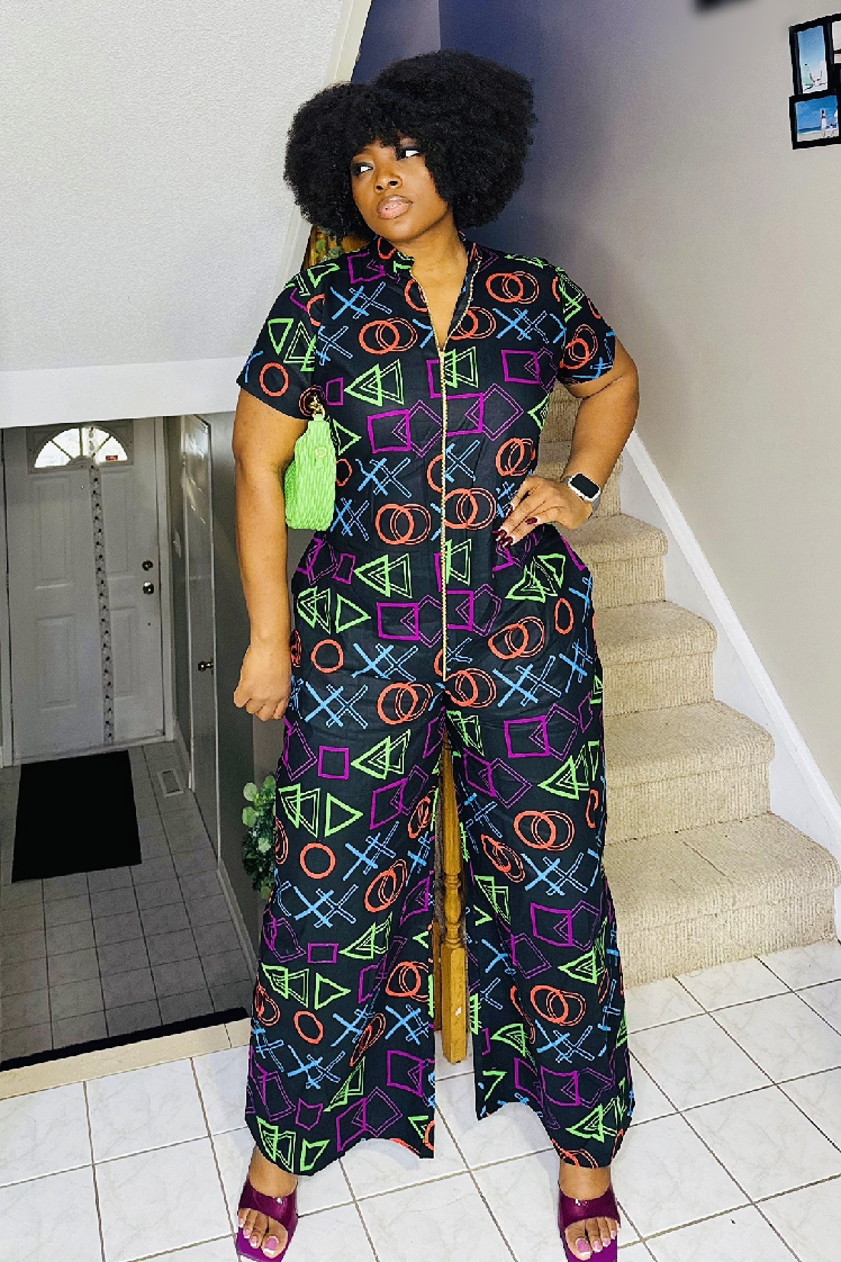 A woman standing on a staircase wearing a colorful African print jumpsuit with a video game-inspired pattern, consisting of various geometric shapes in vibrant colors.