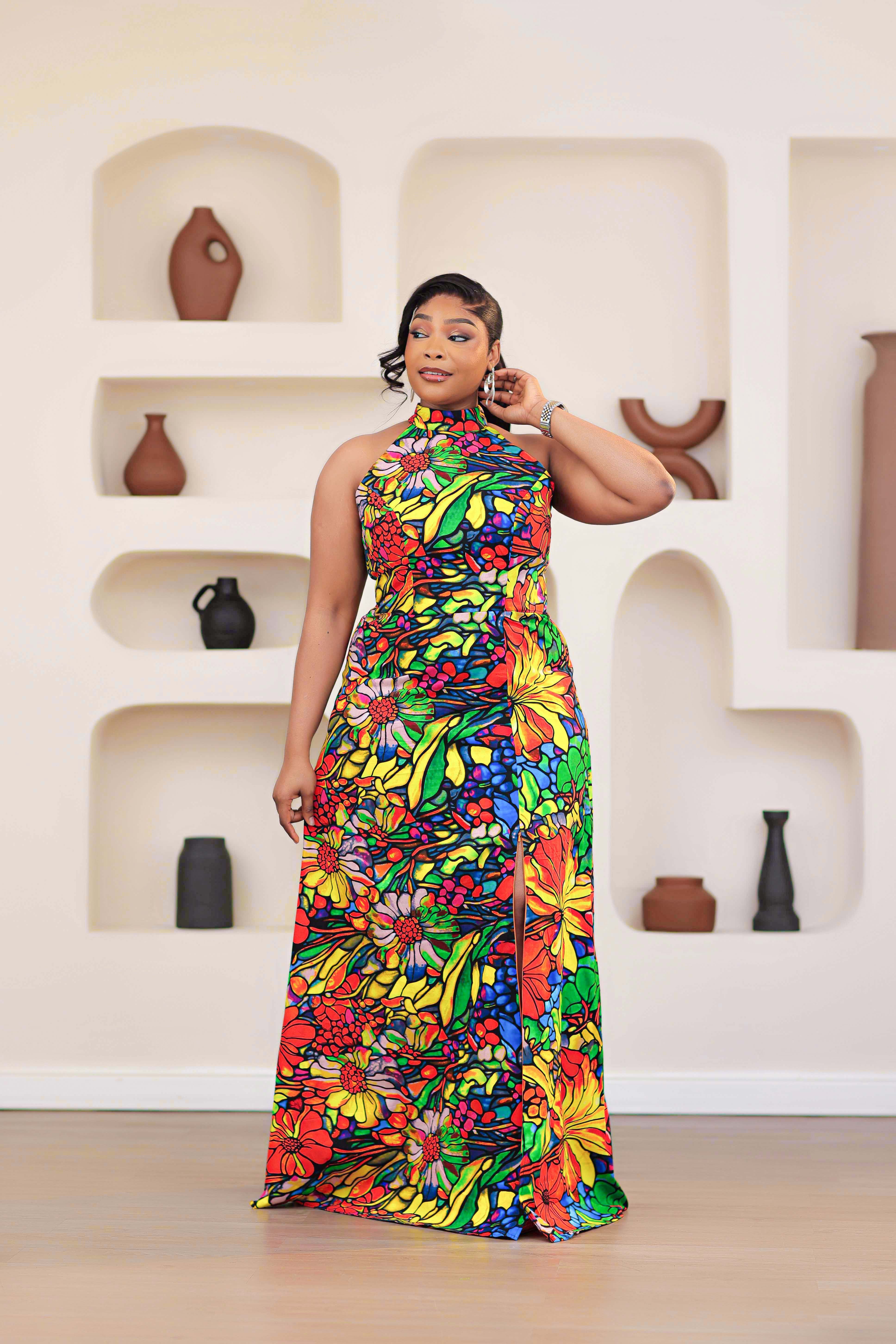 Woman wearing a colorful NIKI KAY African print Ankara multicolor floral dress standing in front of a wall with decorative vases.