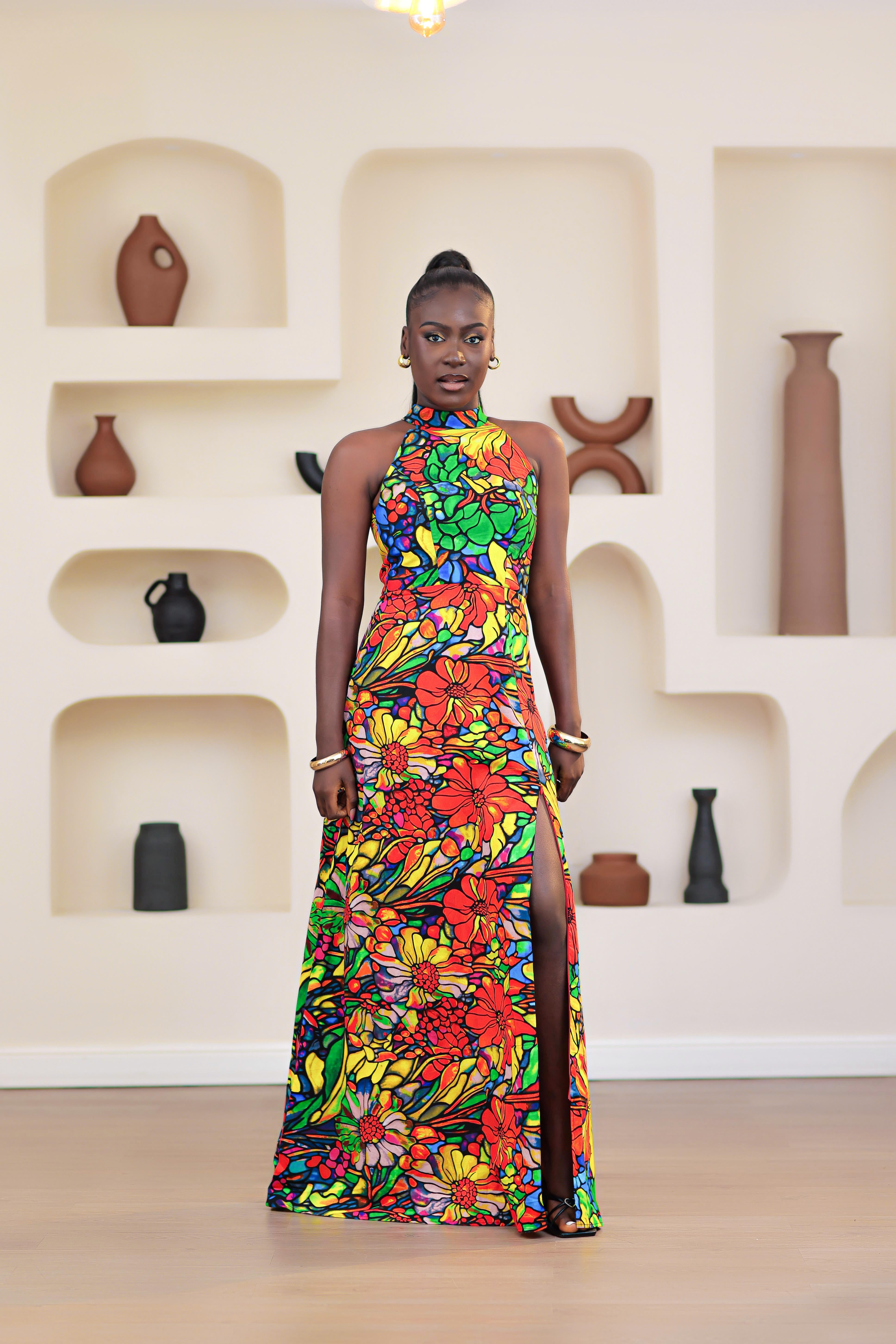 Woman wearing a colorful NIKI KAY African print ankara multicolor floral dress standing in front of a wall with decorative vases.