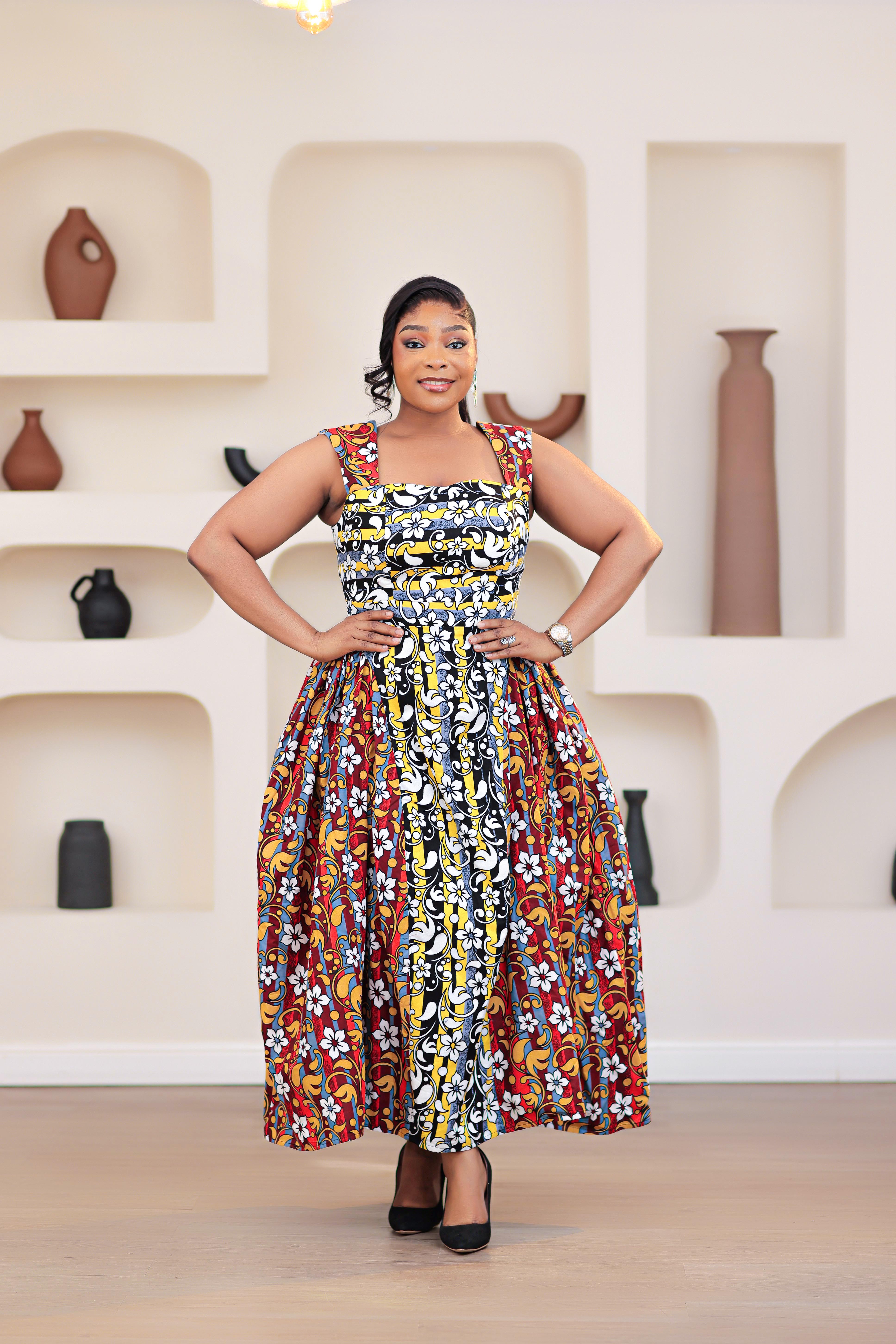 Woman in a colorful patterned mixed prints african print ankara sleeveless dress standing in front of a decorative wall with shelves.