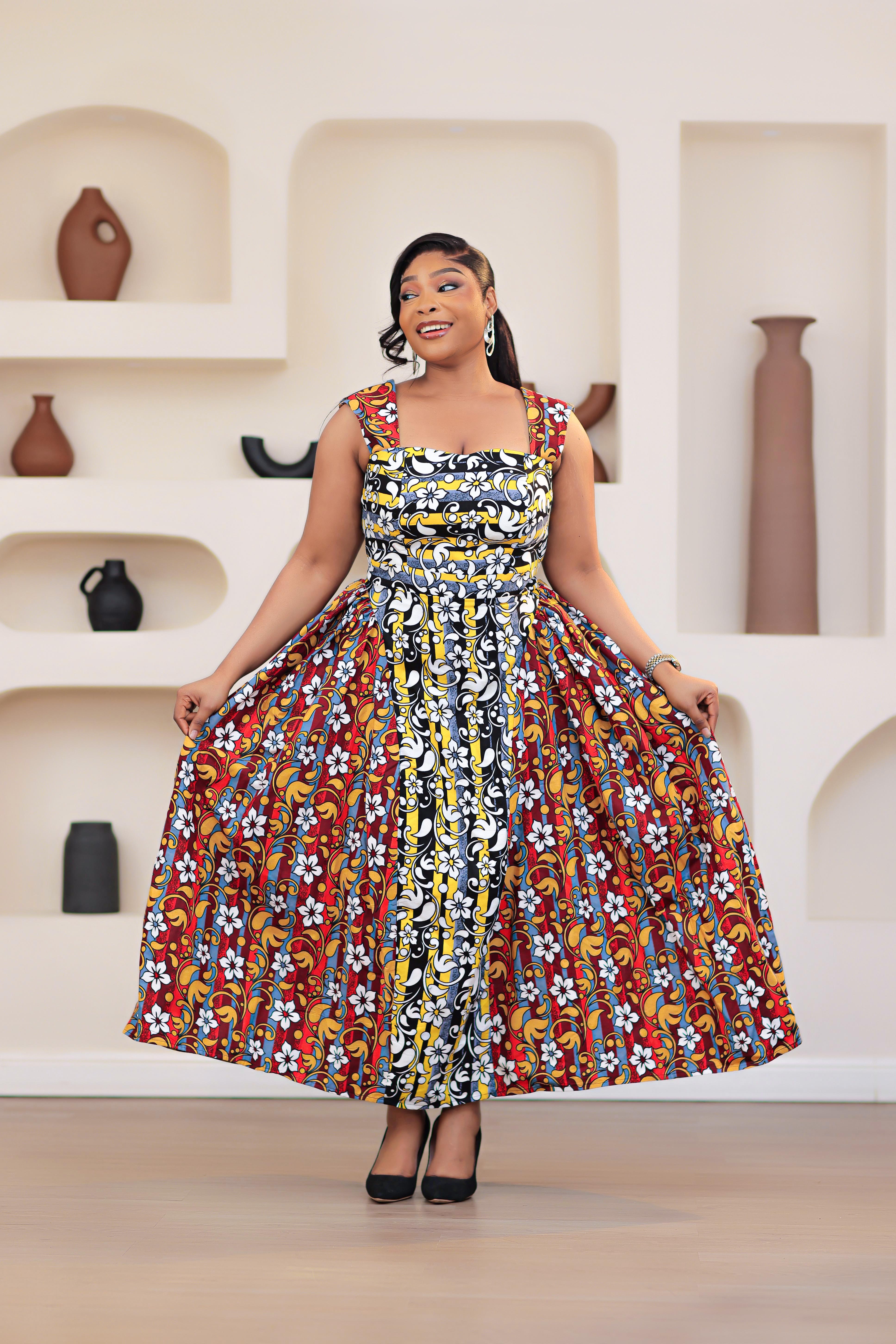 Woman in a colorful patterned mixed prints african print ankara sleeveless dress standing in front of a decorative wall with shelves.