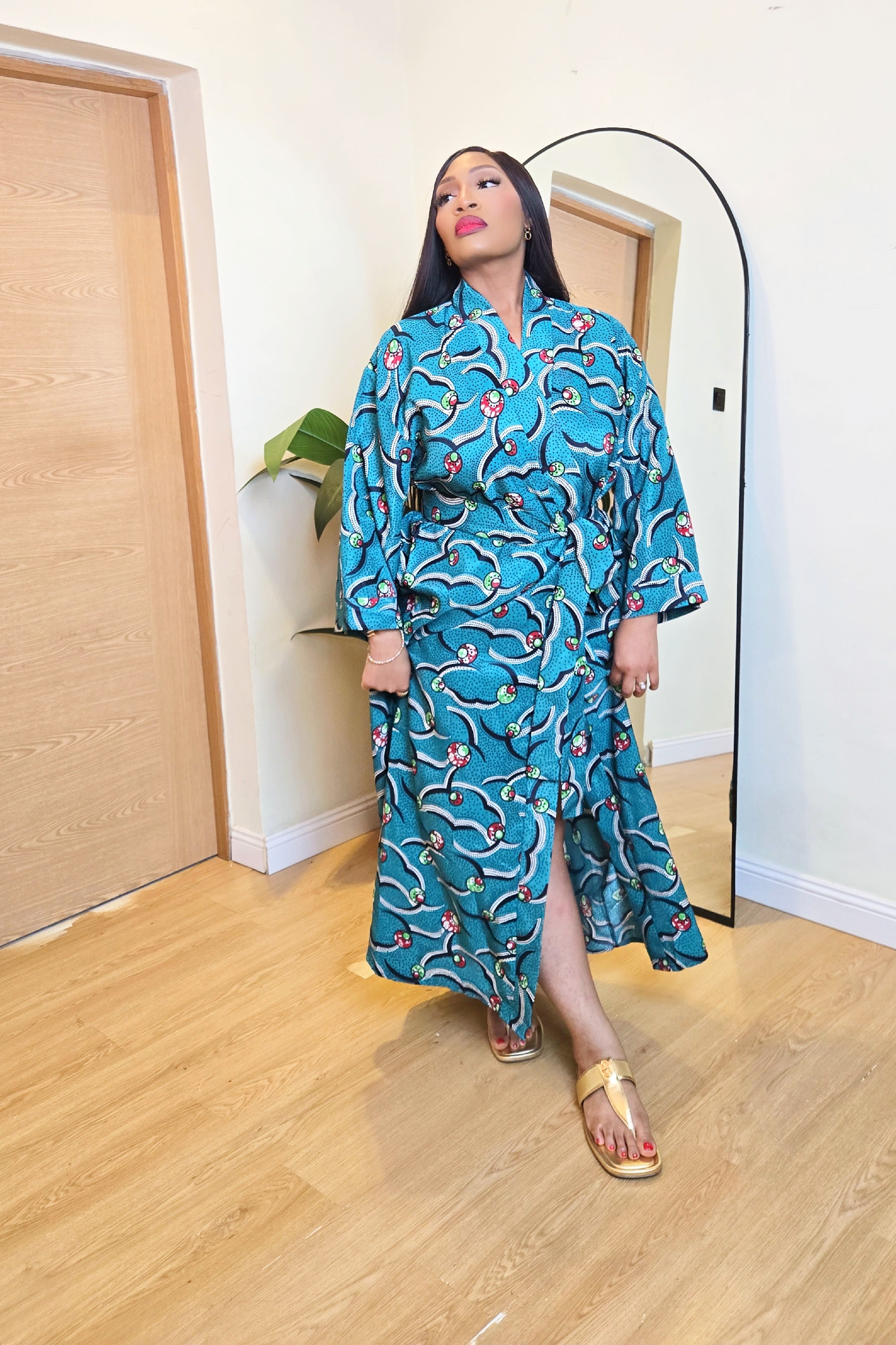 Woman in a teal patterned NIKI KAY African print robe dress standing in a room with wooden flooring.