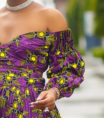 A woman wearing a bold African print Ankara purple and yellow African print wrap top with bubble sleeves and a off-the-shoulder neckline.